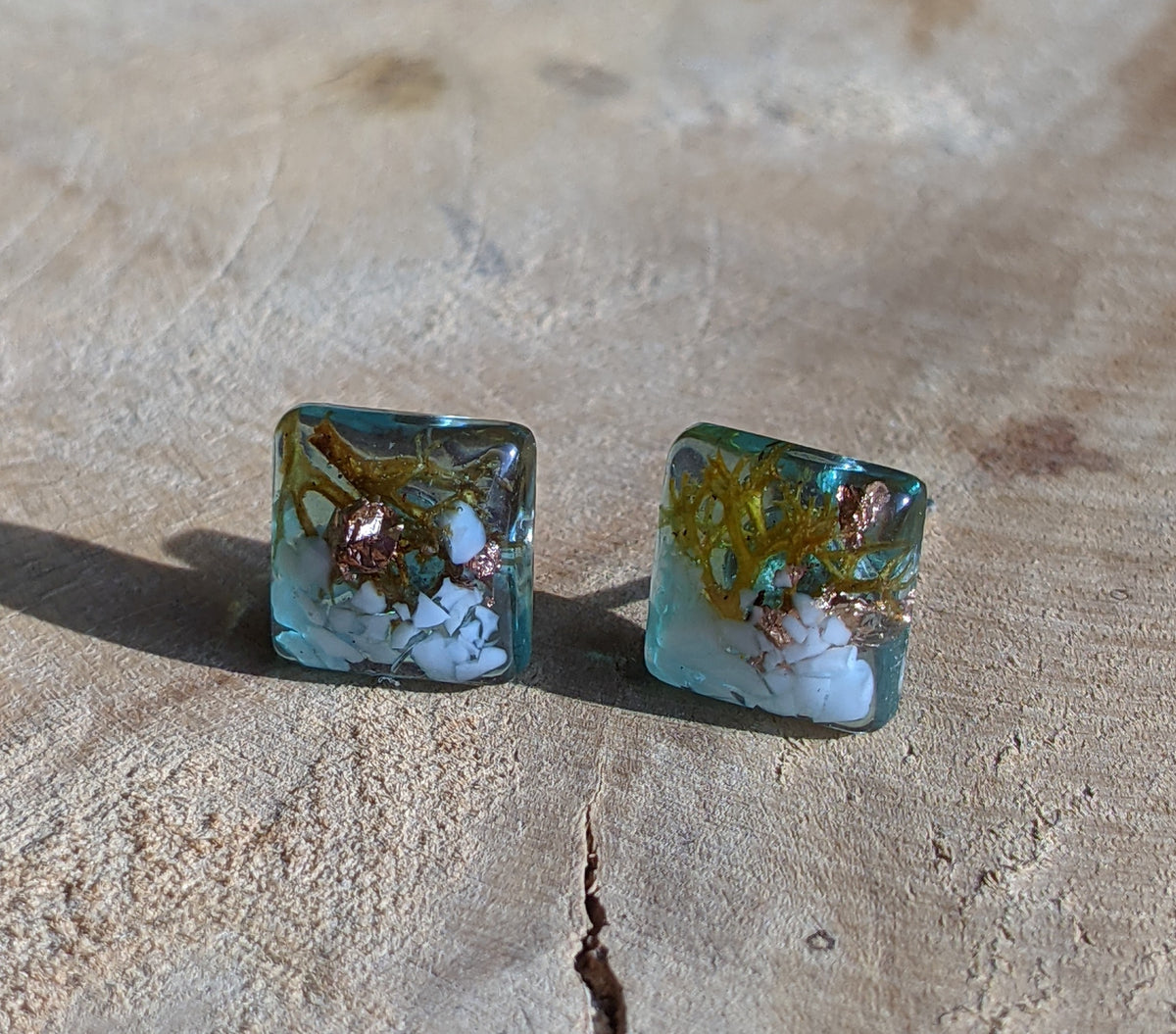 Close-up of white stone moss and copper flakes inside clear resin square stud earrings, EL Creations