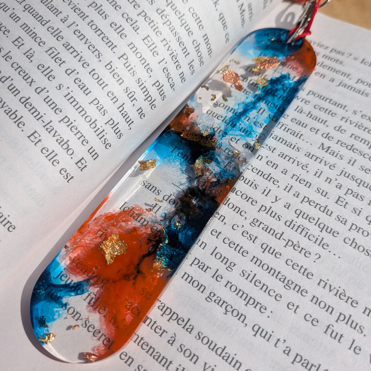 Side angle of burning tide resin bookmark on open book showing mirror-polish and red cord clasp – EL-Creations