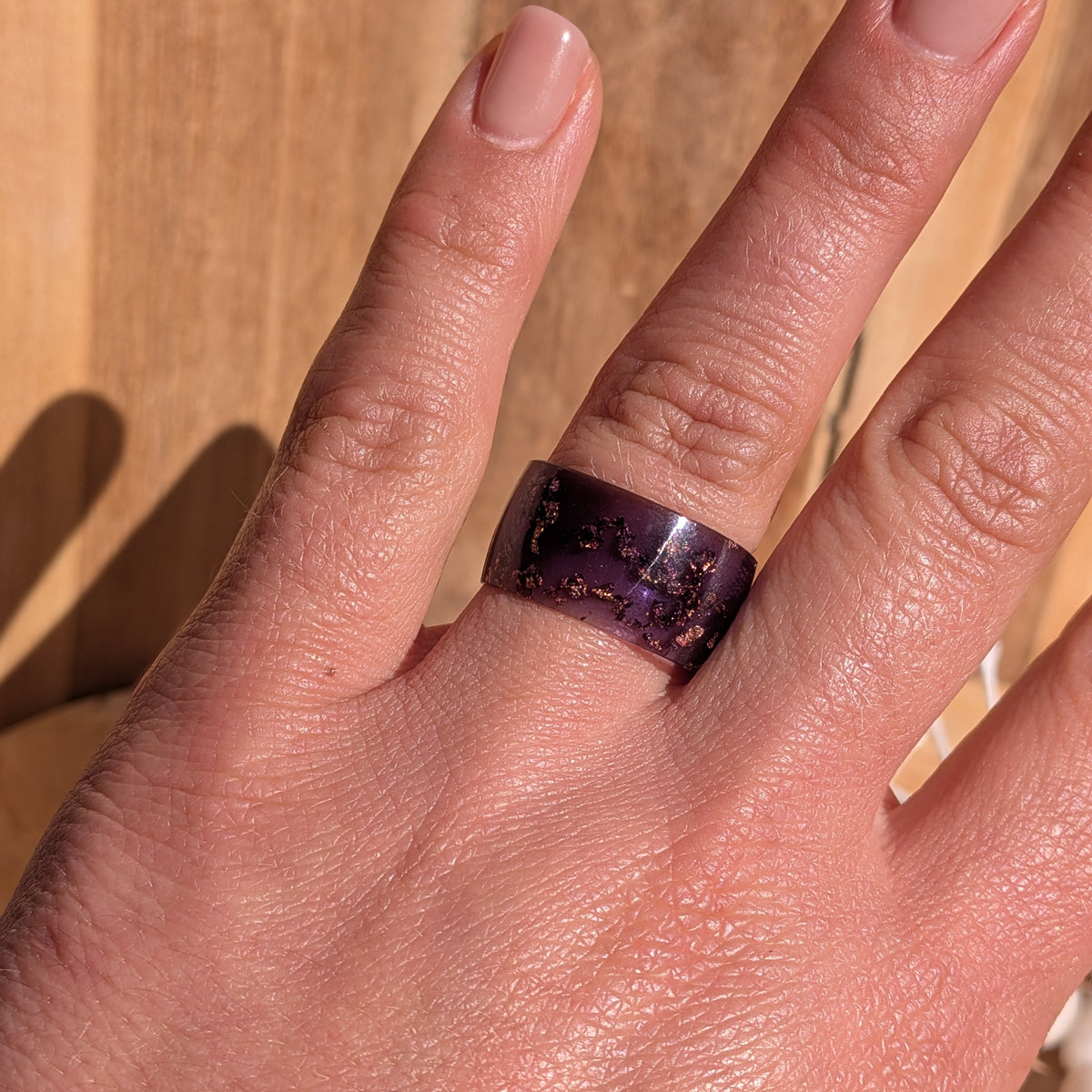 Wide purple resin statement ring with copper flakes worn on a hand against a wooden background, EL-Creations