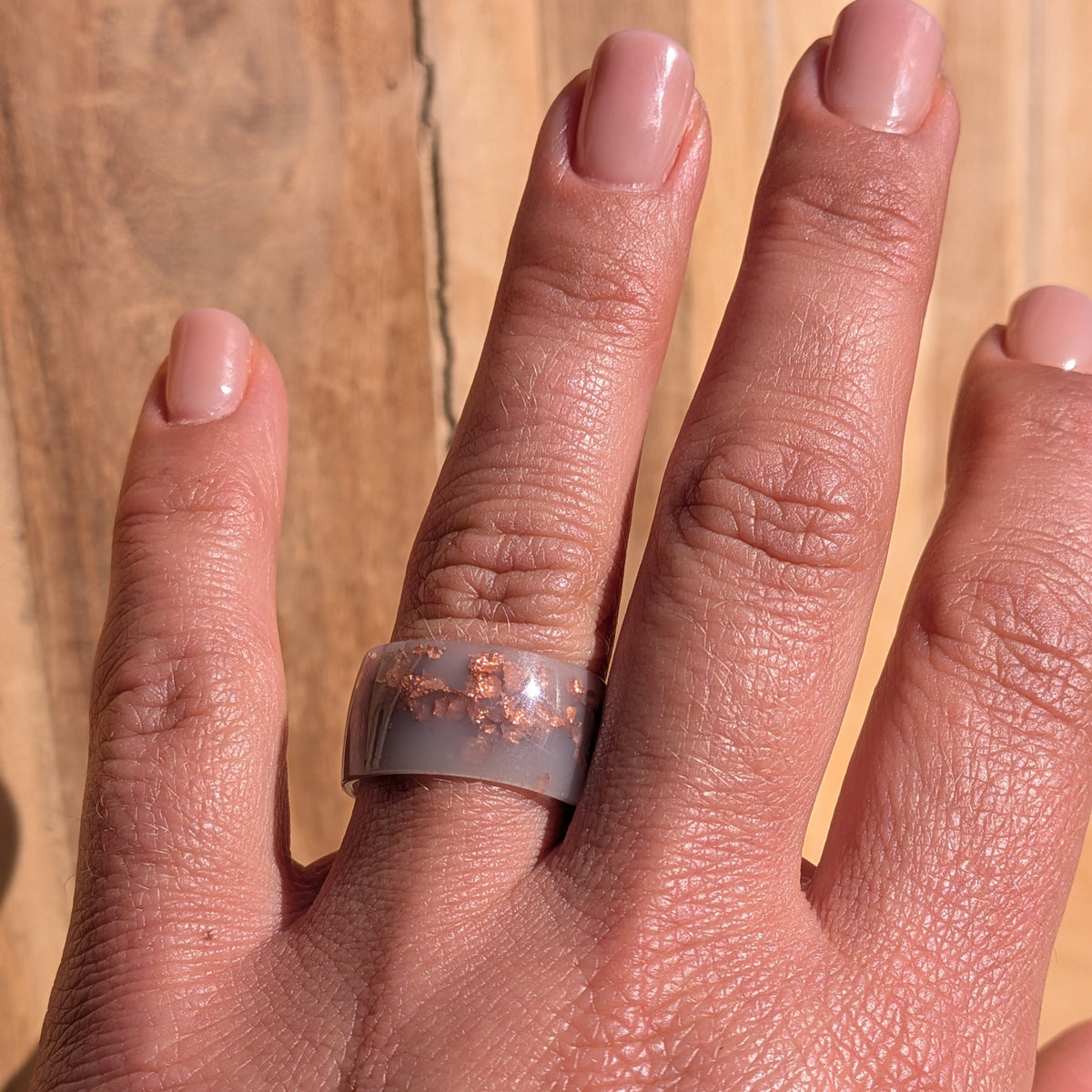 Milky lilac resin statement ring with copper flakes worn on an outstretched hand against a sunlit wooden background, EL-Creations