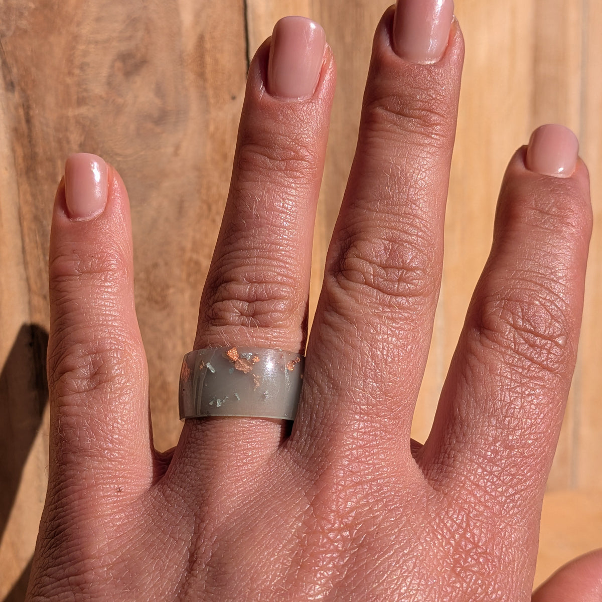 Milky blue-green resin statement ring with silver and copper flakes worn on an outstretched hand against a wooden background, EL-Creations