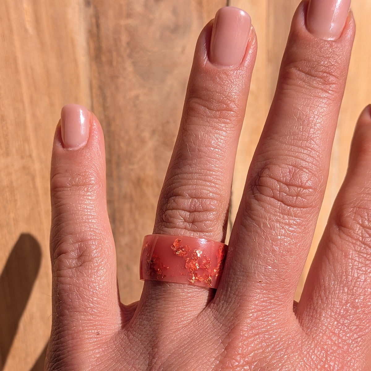 Milky pink resin statement ring with copper flakes worn on a hand against a sunlit wooden background, EL-Creations
