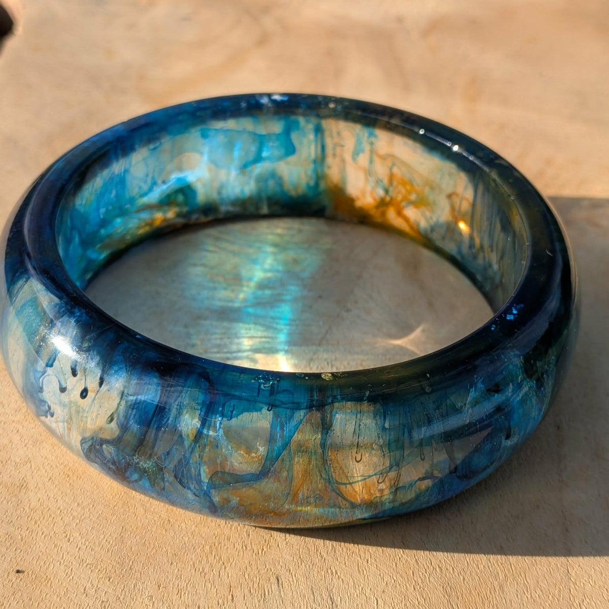 Deep ocean resin bangle top view showing blue teal and gold swirl pattern on wood – EL-Creations