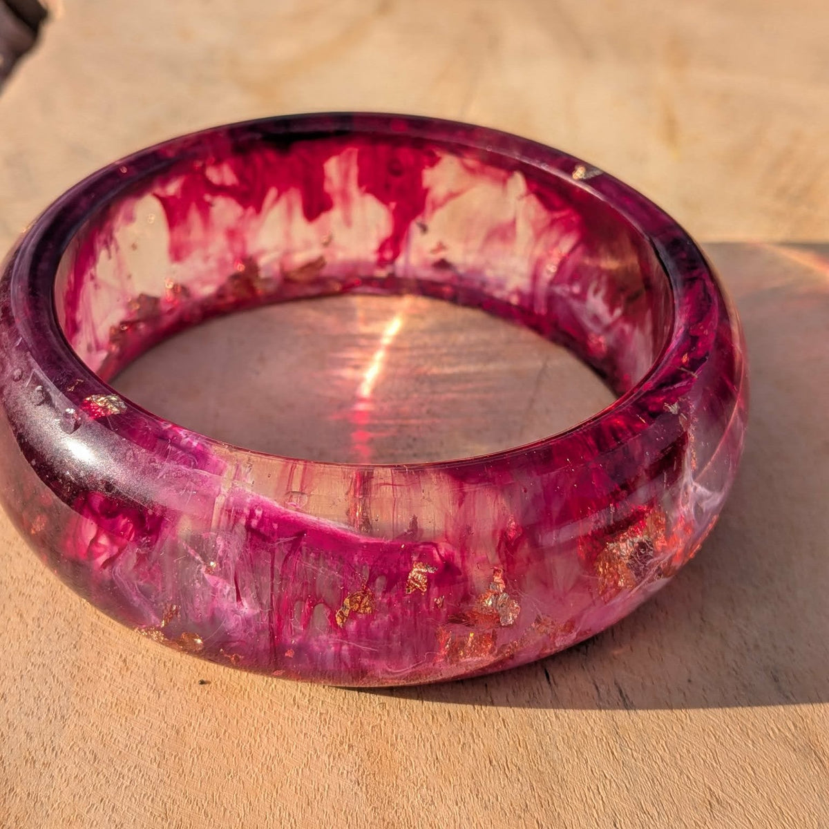 Top view of wild berry resin bangle on wooden surface showing burgundy rose gold swirl pattern – EL-Creations