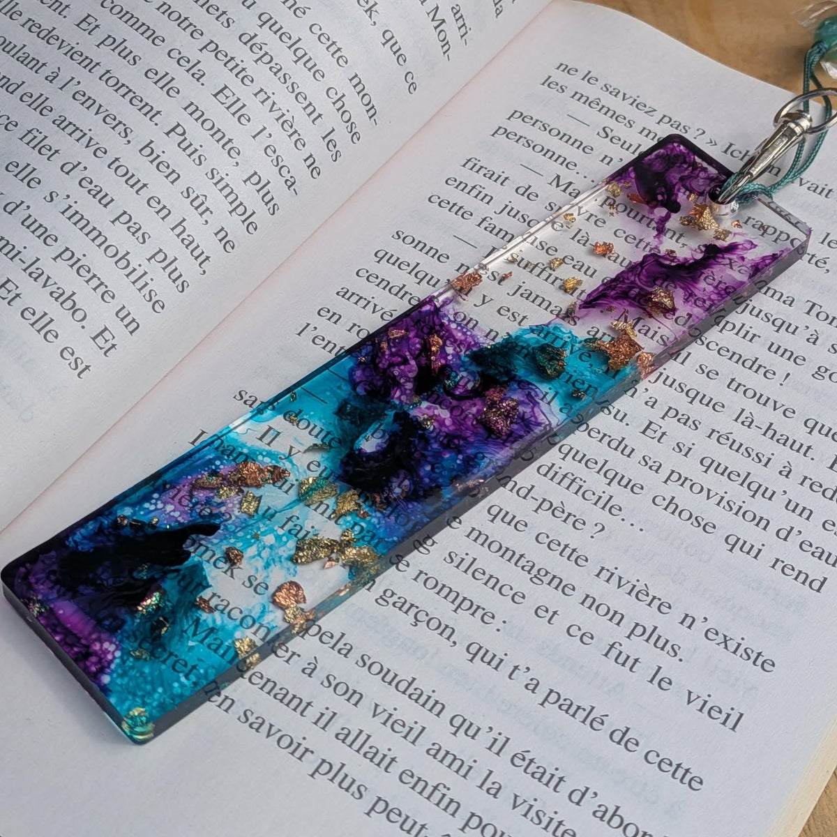 Close-up of purple and teal resin bookmark with lobster clasp and teal tassel on book – EL-Creations