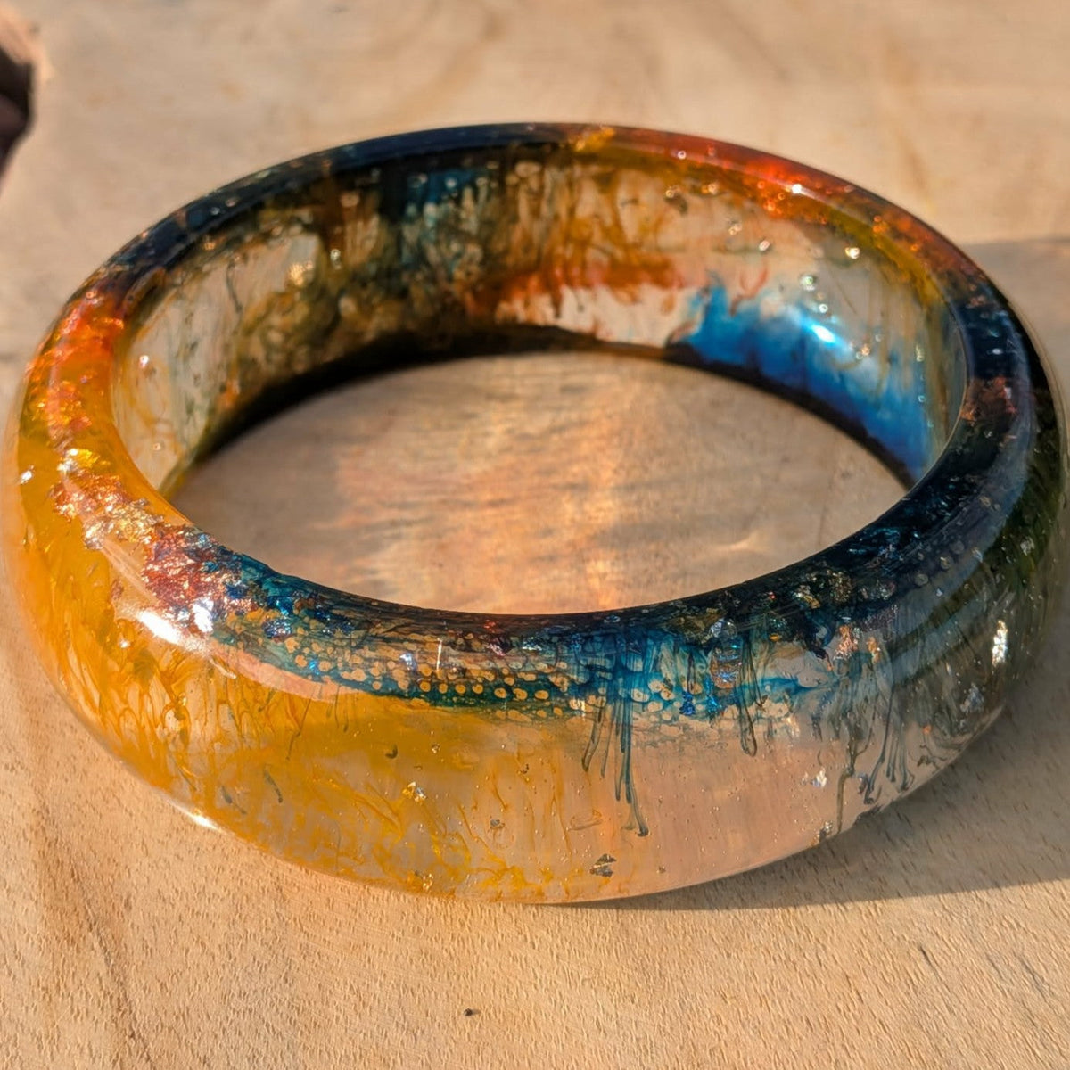 Handmade amber orange resin bangle with teal swirls worn on wrist in sunlight – EL-Creations