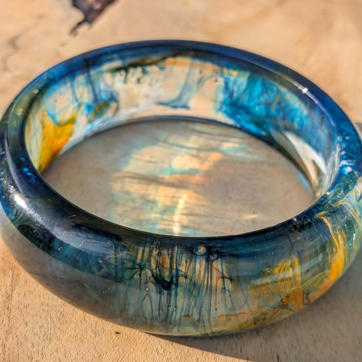 Three quarter view of ocean blue resin bangle with teal and gold detail on wood – EL-Creations