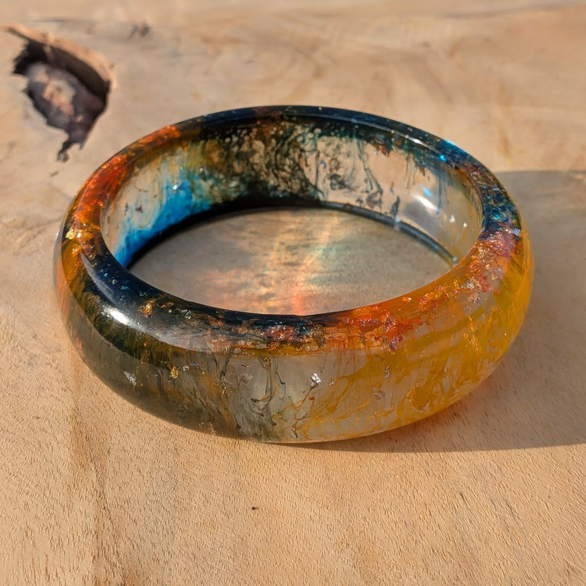 Amber tide resin bangle worn on wrist showing orange and teal glow against brick wall – EL-Creations