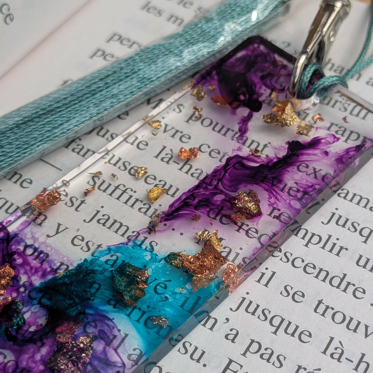 Top view of teal purple resin bookmark with gold and copper leaf on open book – EL-Creations