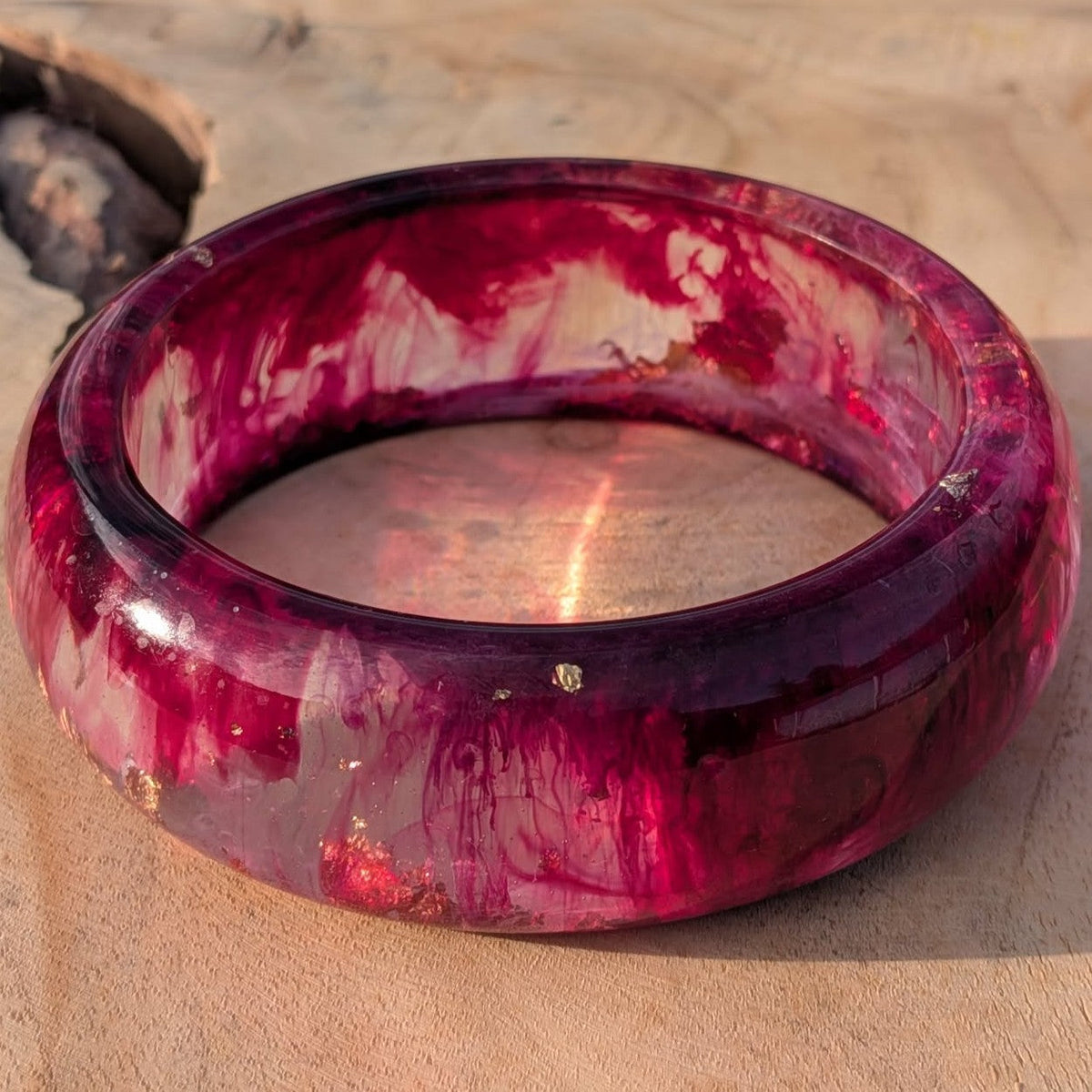 Angled view of deep burgundy raspberry resin bangle with gold silver leaf on wood – EL-Creations