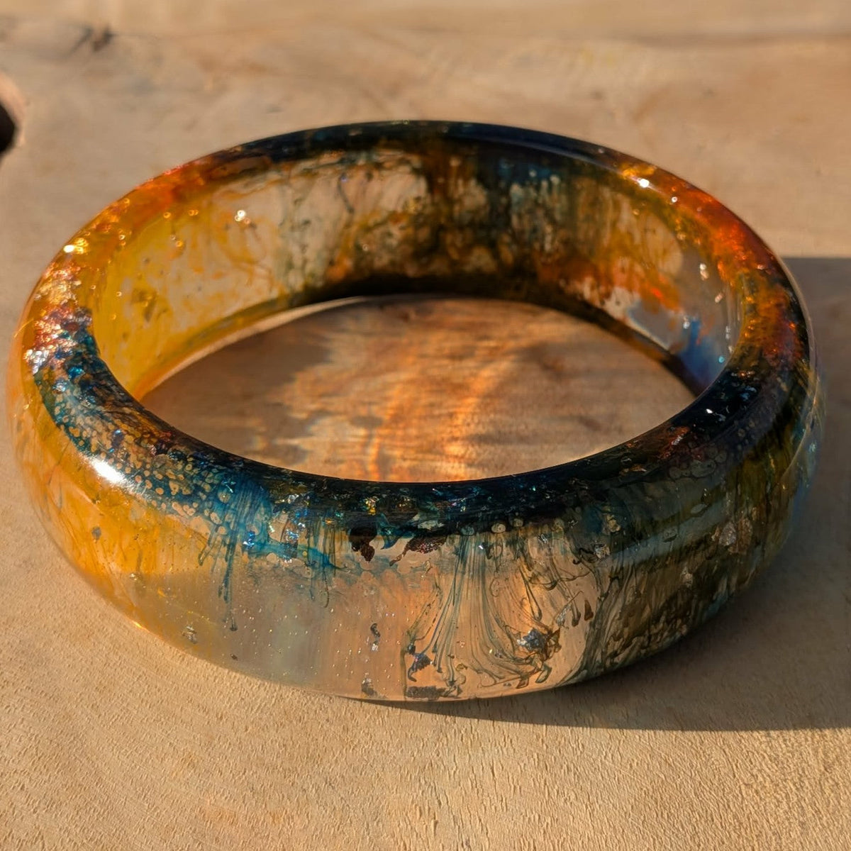 Top view of amber orange epoxy resin bangle with teal and gold swirls on wooden surface – EL-Creations