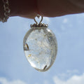 Clear teardrop-shaped pendant with dried flowers against a blue sky background