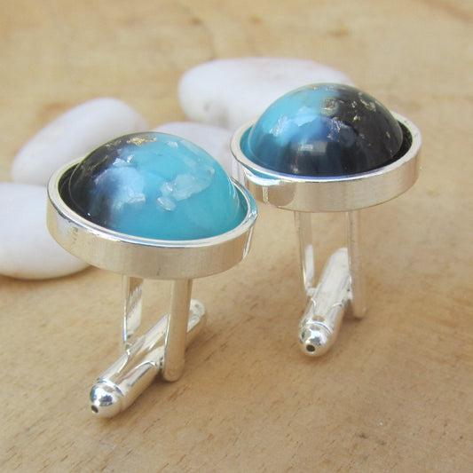Silver cufflinks with blue and black gemstones on a wooden surface