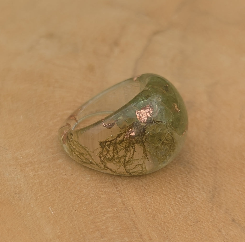 Ring with green stone and copper accents on a beige surface