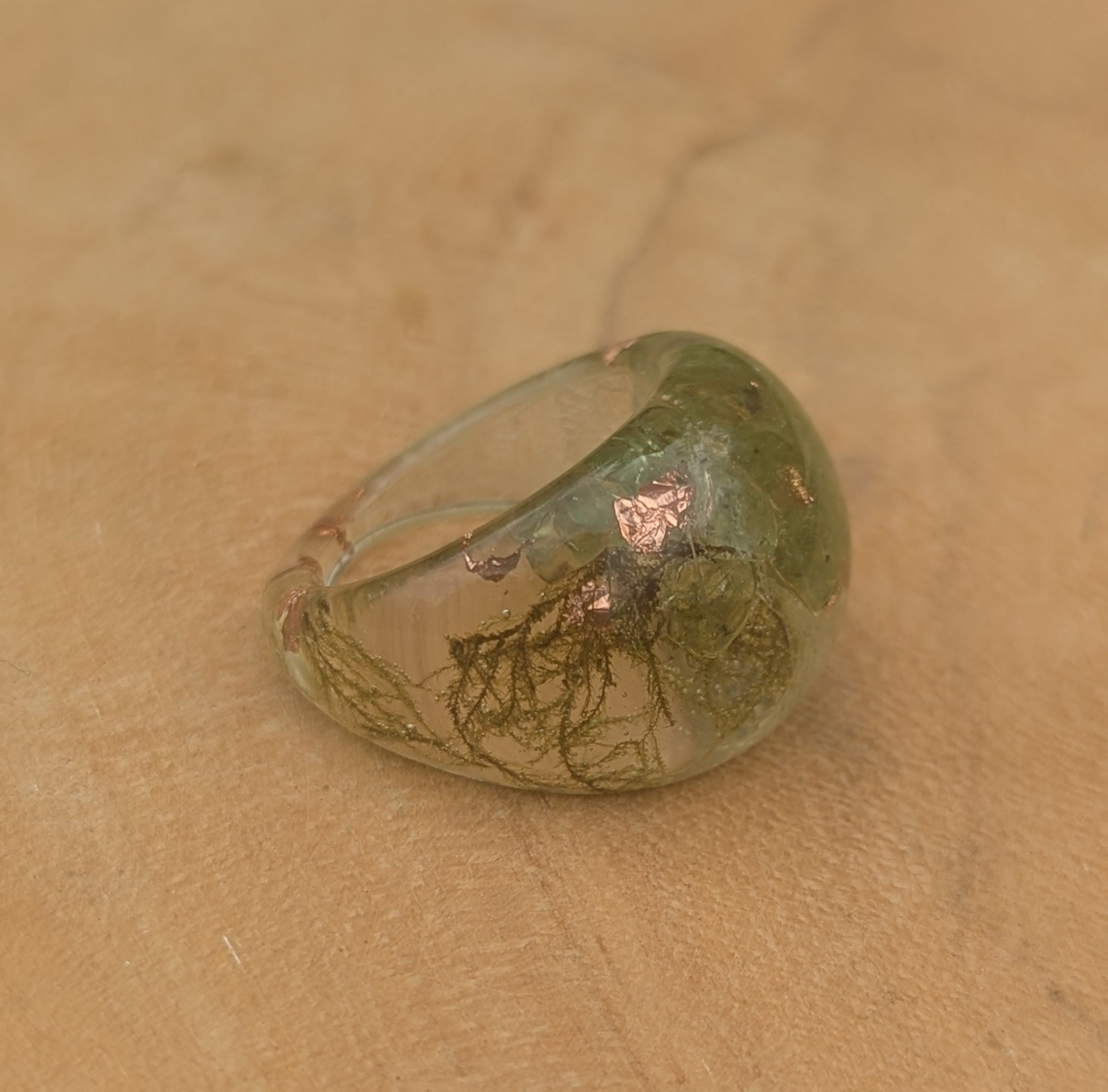 Ring with green stone and copper accents on a beige surface