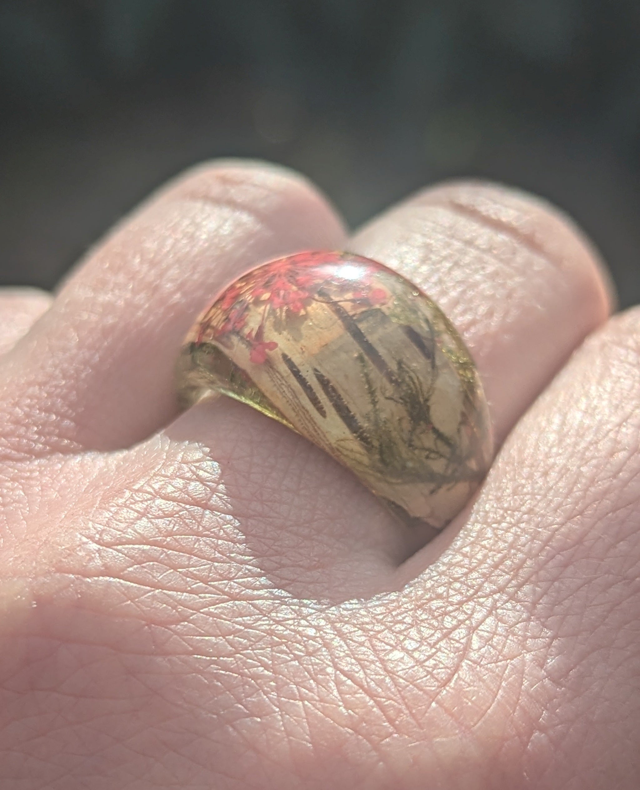 Ring with floral design worn on a finger against a blurred background