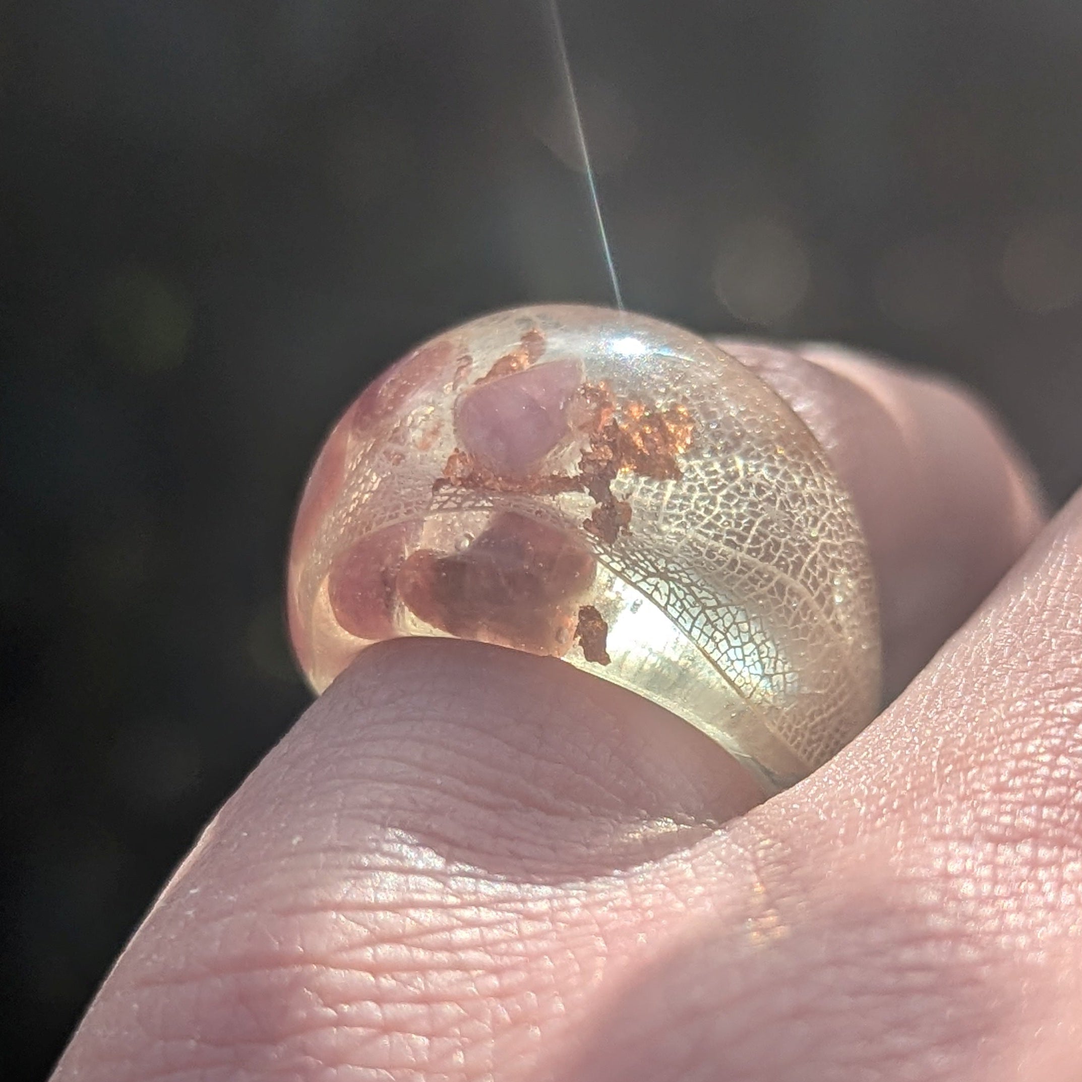 Close-up of a hand holding a transparent bubble with a small insect inside against a dark background