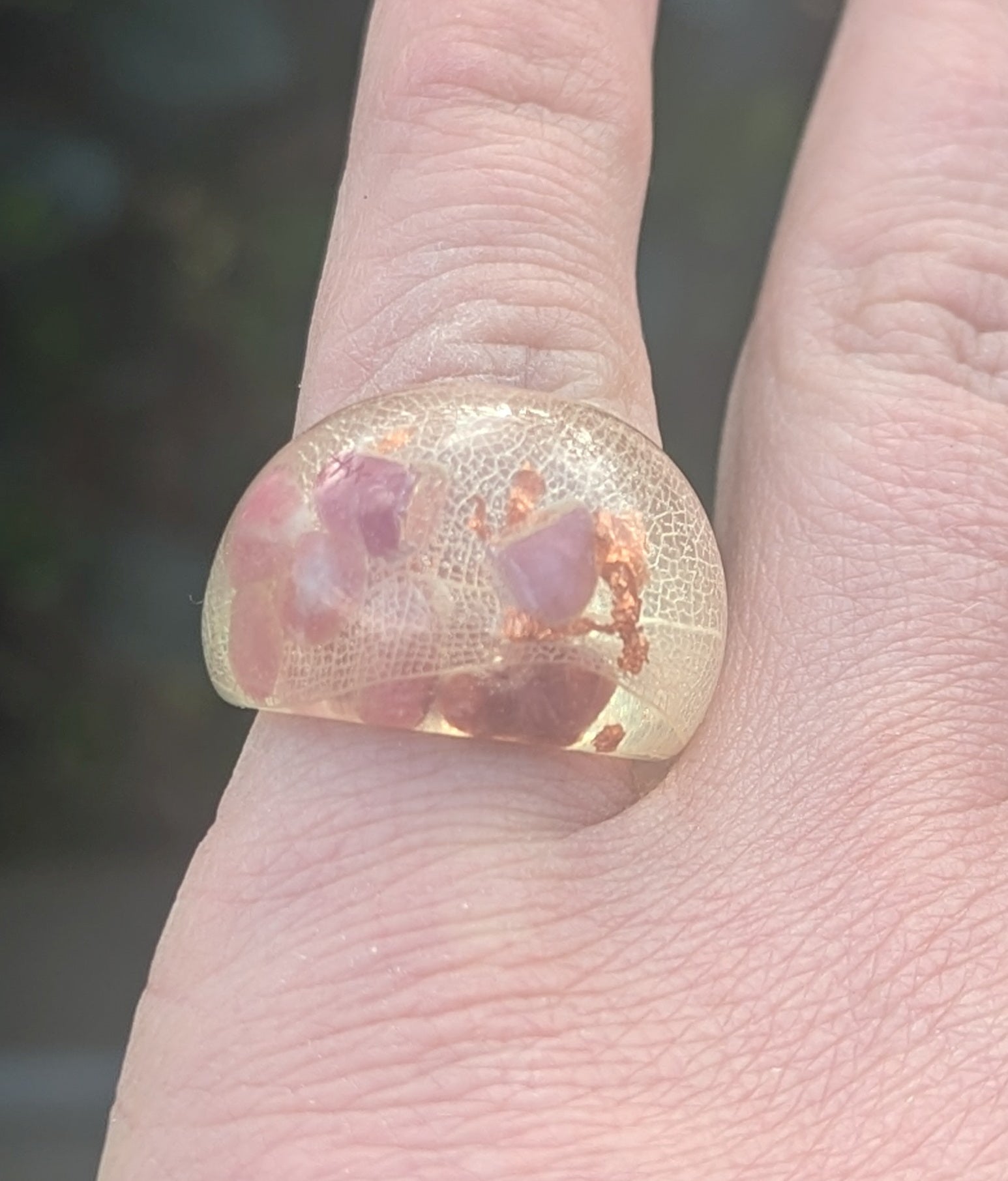 Resin ring with pink stones on a finger against a blurred background