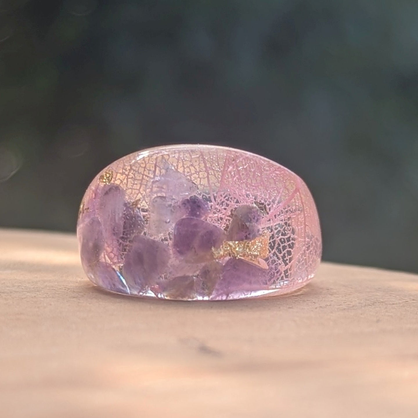 Pink and purple resin ring with embedded flowers on a wooden surface