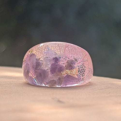 Pink and purple resin ring with embedded flowers on a wooden surface