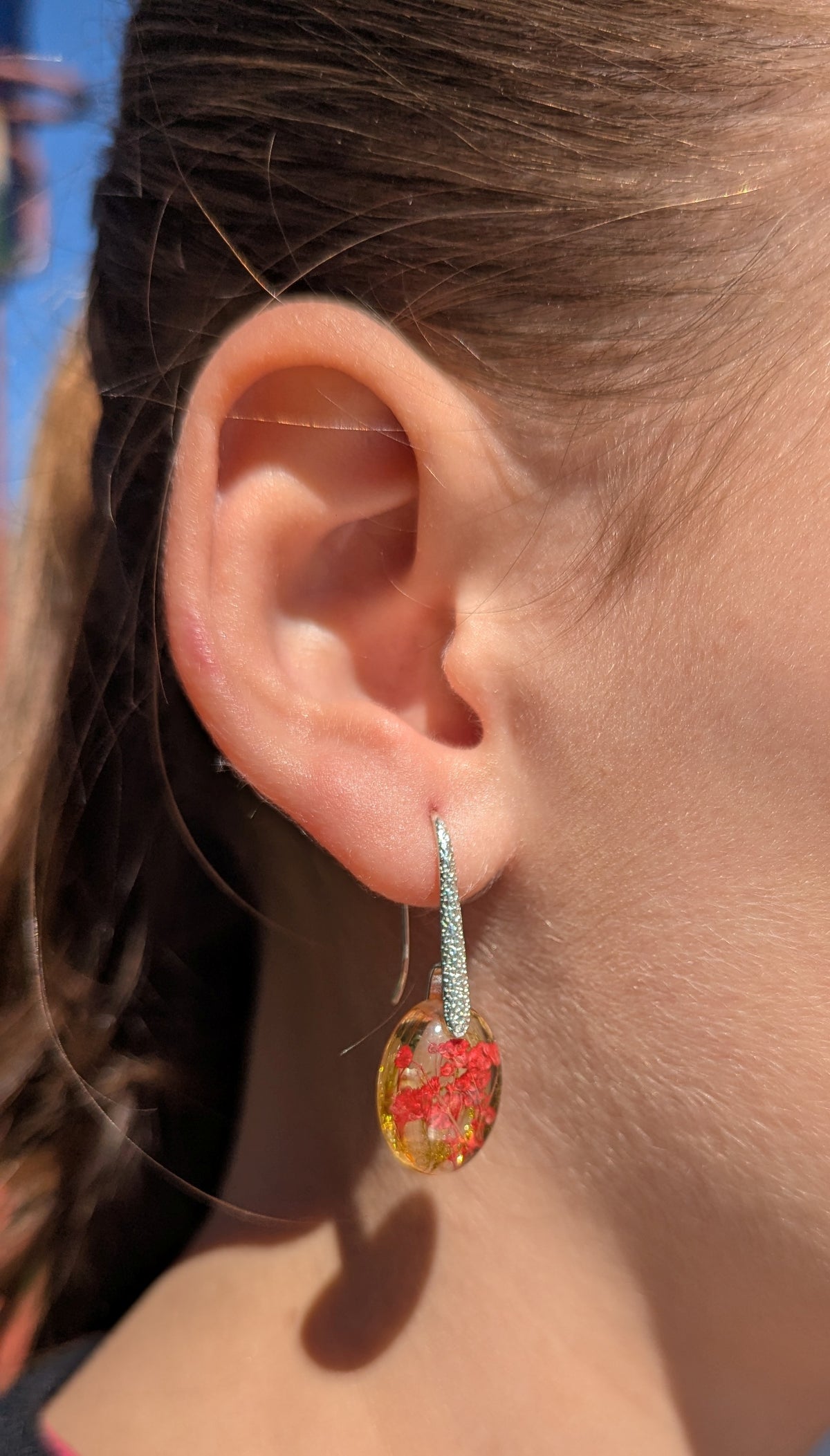 Handmade red flower moss resin oval earrings worn on ear against blue sky, botanical jewelry EL Creations