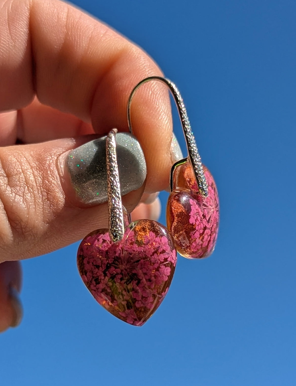 Purple flower heart resin earrings top view on stone surface, botanical jewelry Belgium