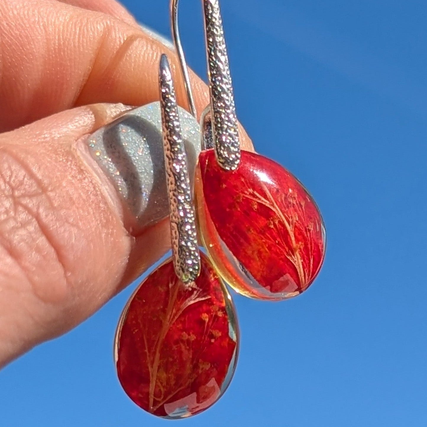 Red earrings with silver hooks held against a blue sky