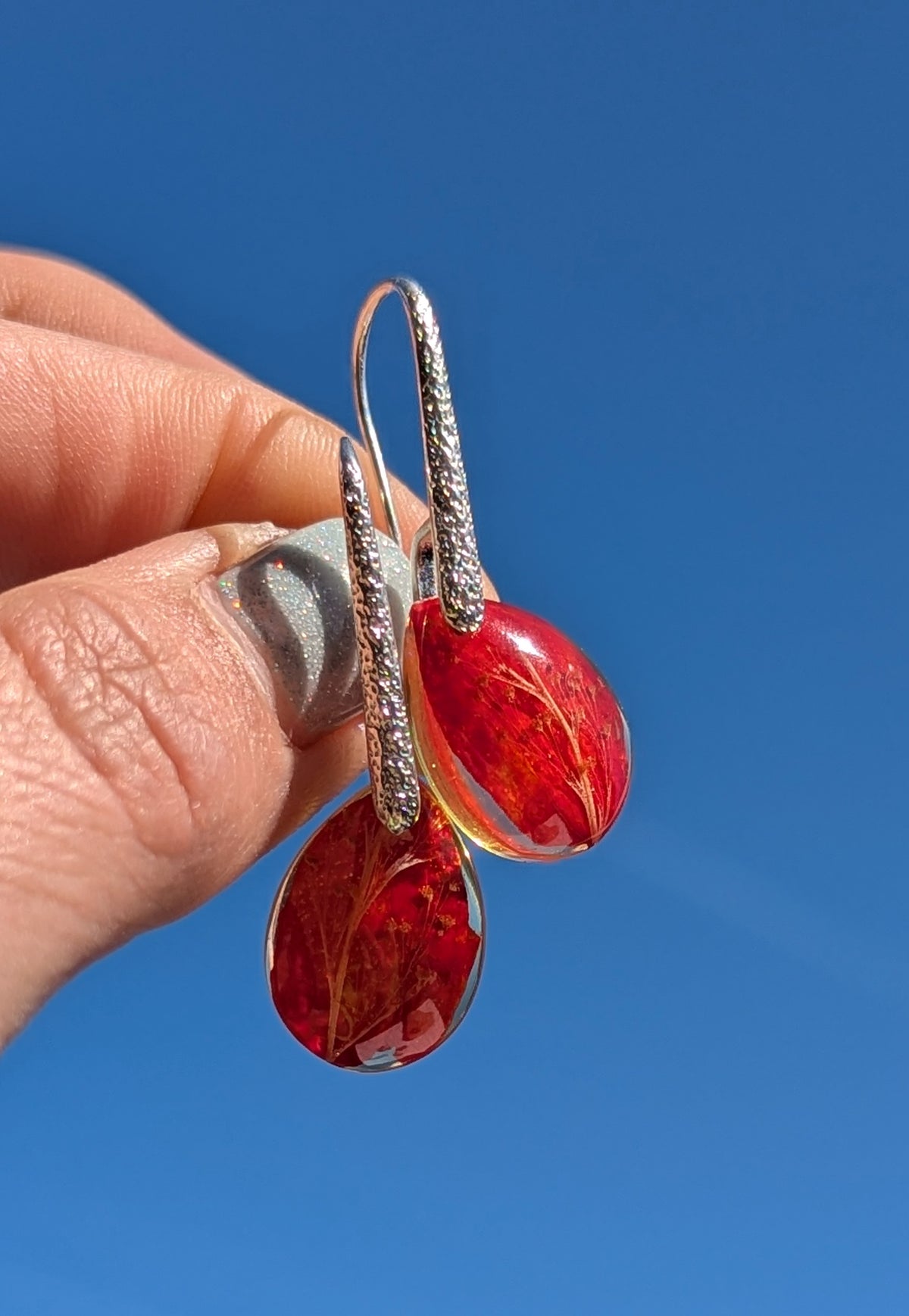 Handmade red botanical drop earrings worn on ear against blue sky, EL Creations Belgium