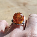 Ring with a large amber stone held in a hand against a blurred background