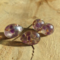 Four purple gemstones with copper inclusions on a beige stone surface