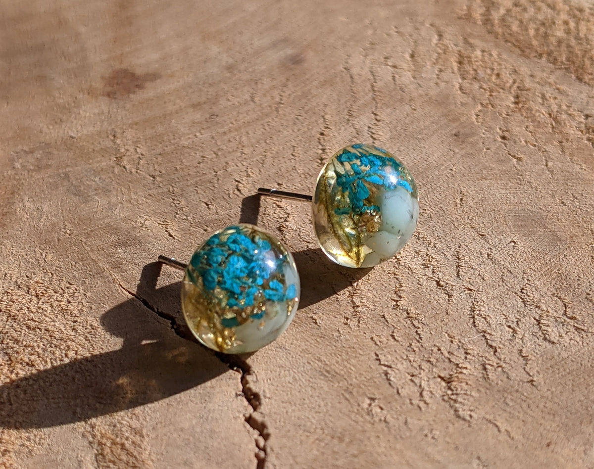 Aquamarine flower resin stud earrings with gold flakes on stone surface, EL Creations