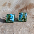 Square green earrings with blue floral design on a beige surface
