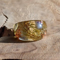 Clear resin ring with embedded natural elements on a wooden surface