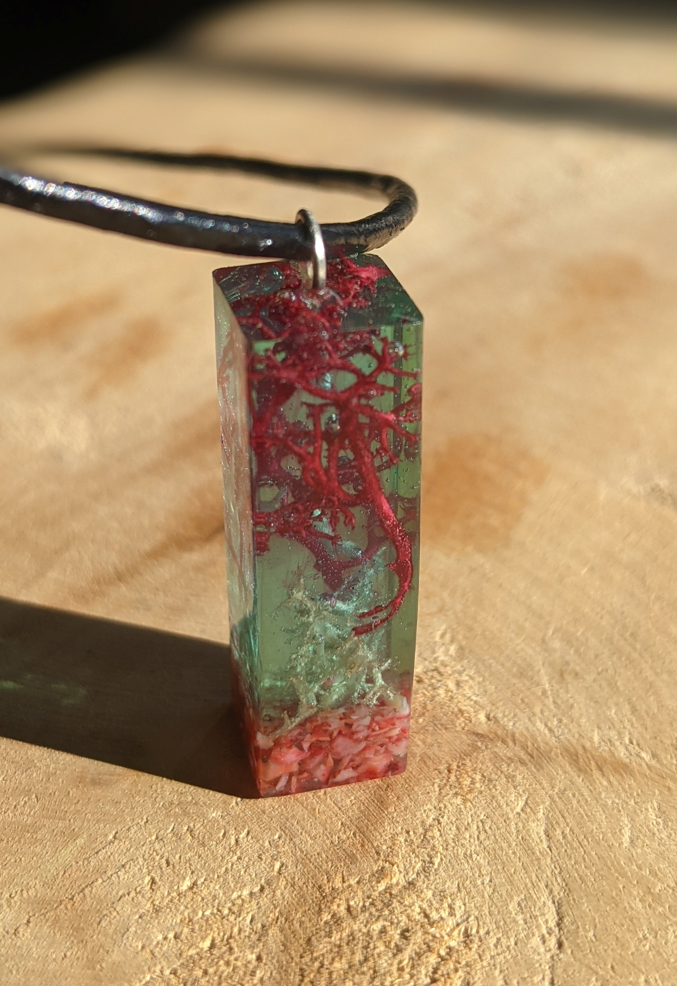 Collier rectangulaire en résine, corail rouge et mousse, avec cordon en cuir ajustable.