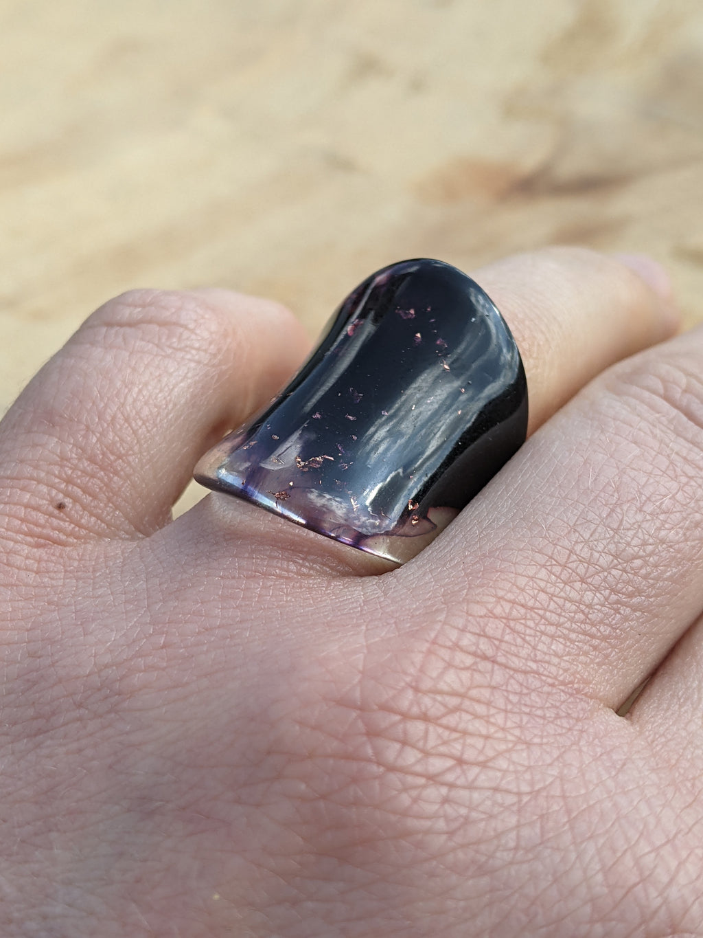 Hand holding a large purple crystal or gemstone against a blurred natural background