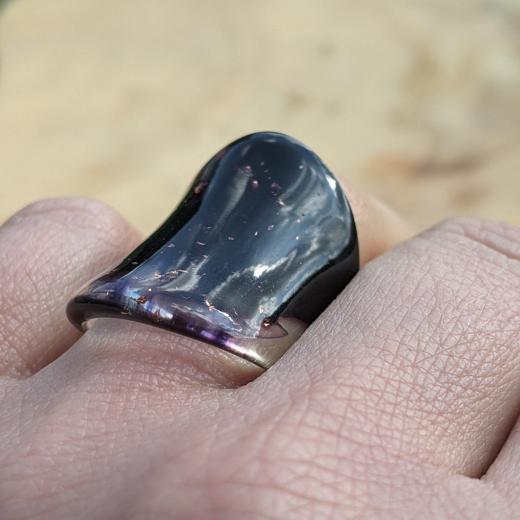 Black ring with a metallic sheen on a finger against a blurred natural background