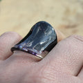 Black ring with a metallic sheen on a finger against a blurred natural background