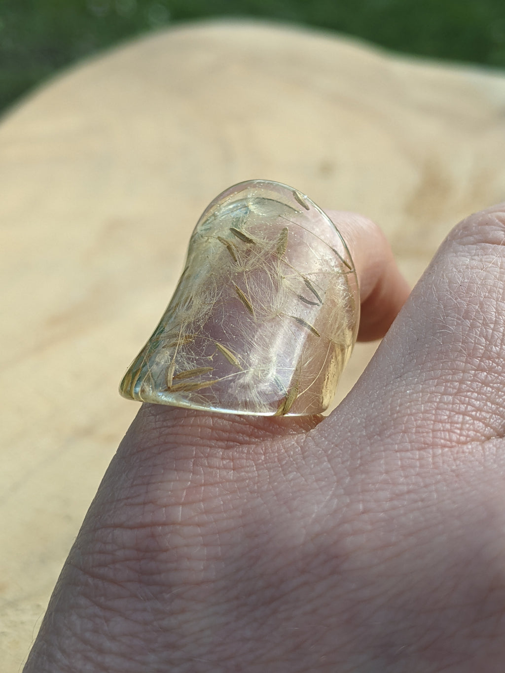 Clear gemstone held between fingers against a blurred natural background