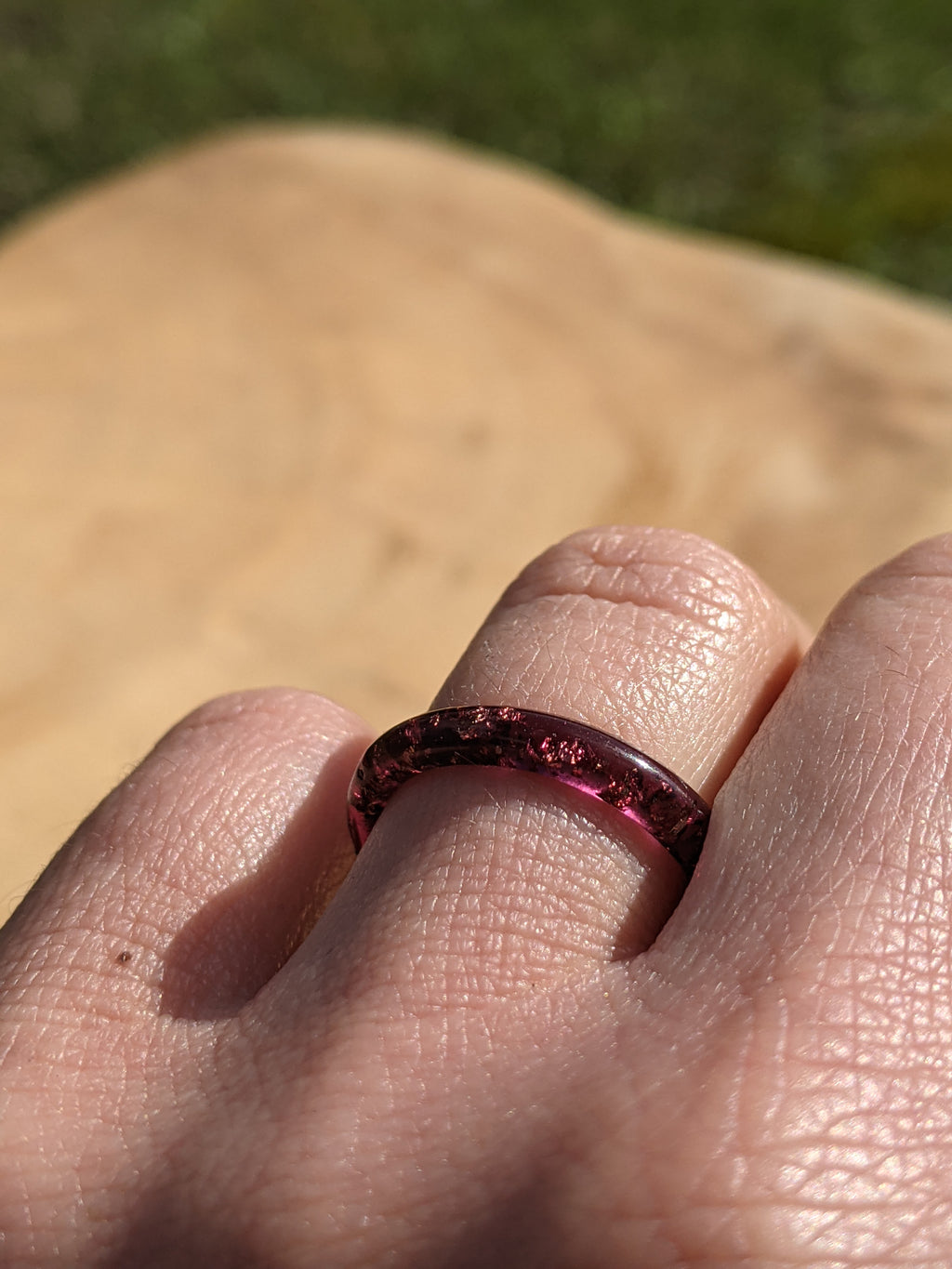 Close-up of a person's finger wearing a red gemstone ring with a blurred natural background