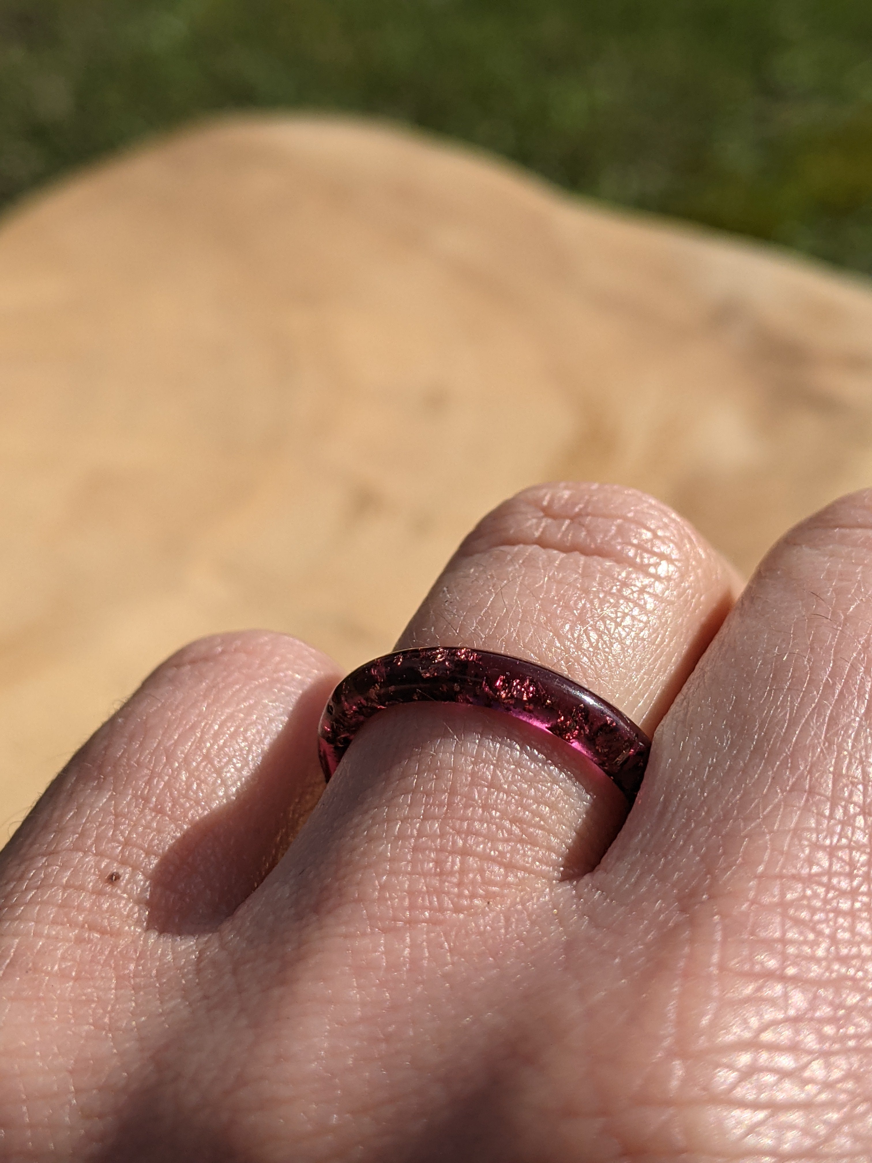 Close-up of a person's finger wearing a red gemstone ring with a blurred natural background