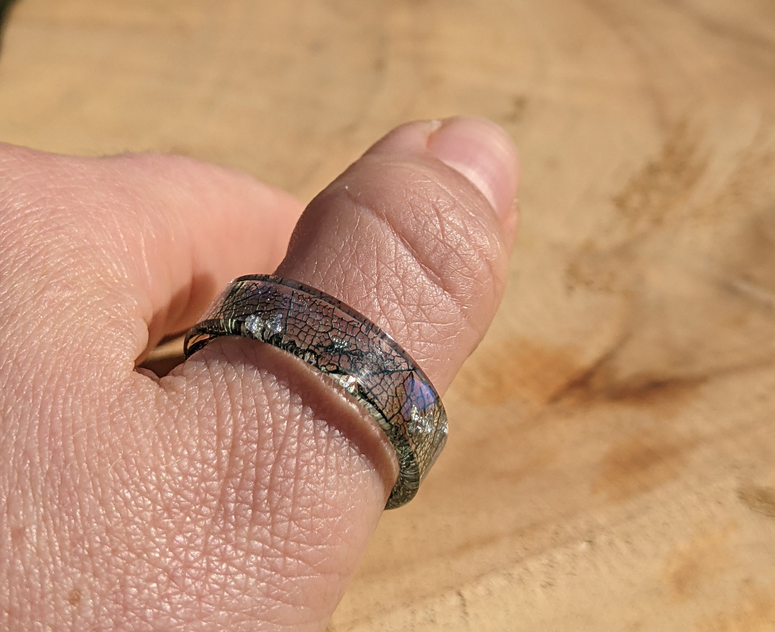Hand wearing a ring with a textured band on a wooden surface