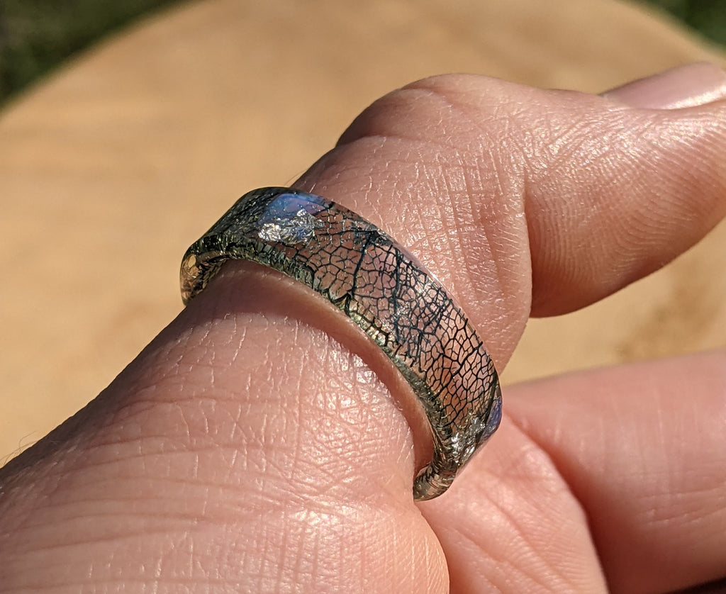 Close-up of a hand wearing a unique, patterned ring with a blurred background.