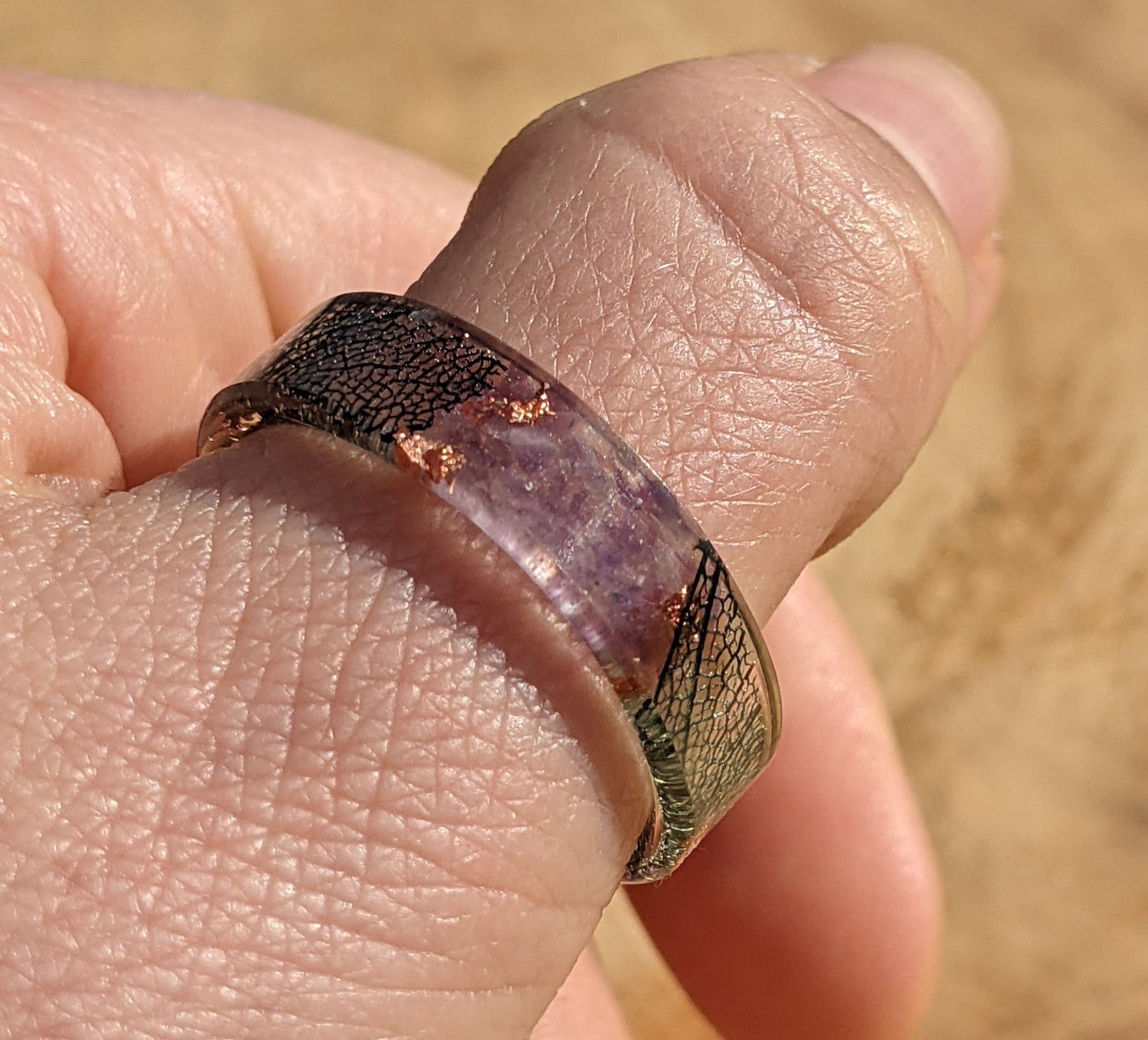 Close-up of a hand wearing a ring with a textured band and purple stone.