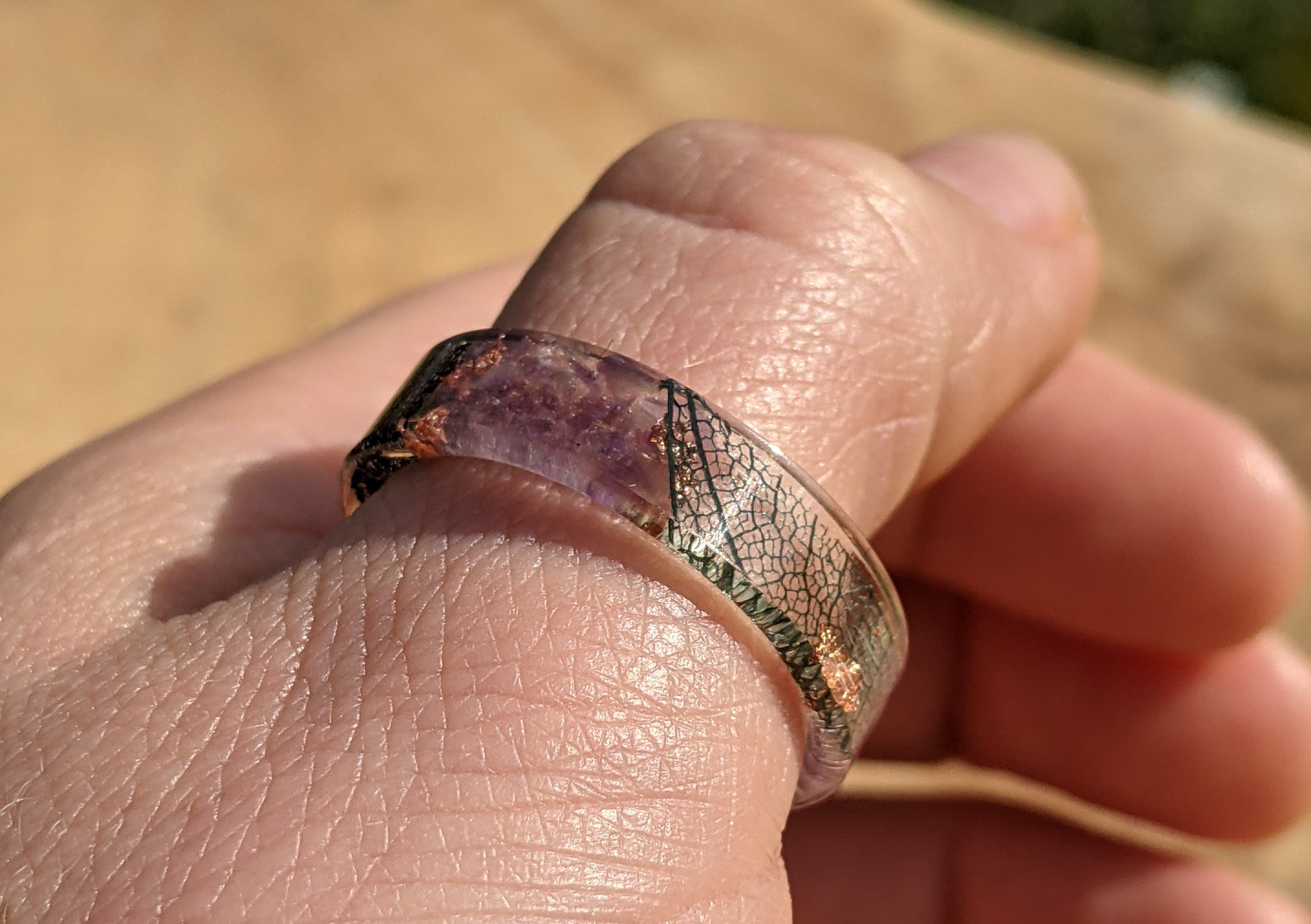 Close-up of a hand wearing a ring with a natural, possibly gemstone, band.