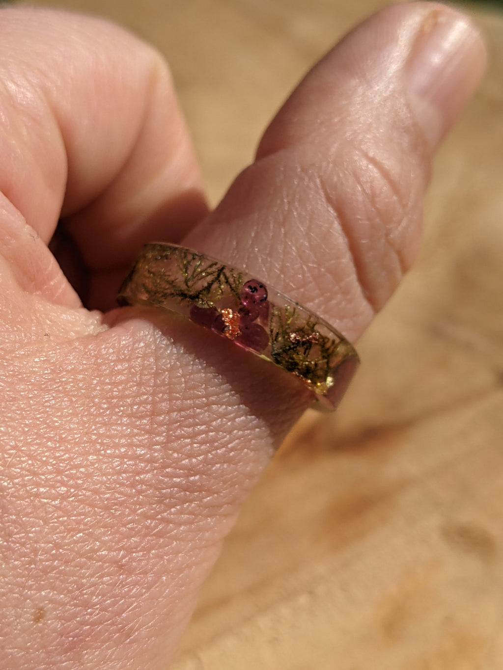 Close-up of a hand wearing a ring with a floral design on a wooden surface