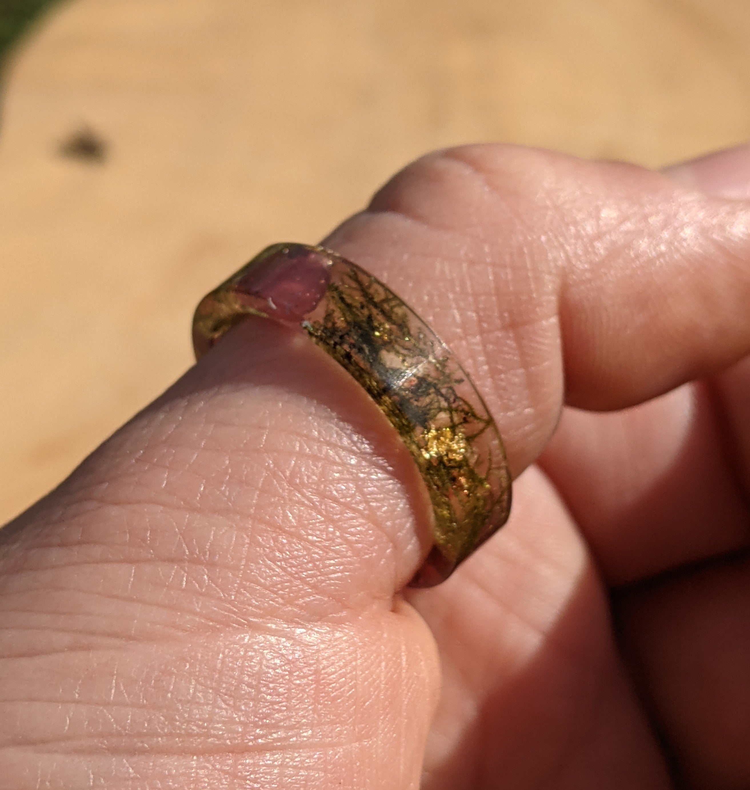 Close-up of a hand wearing a ring with a multicolored gemstone against a blurred background