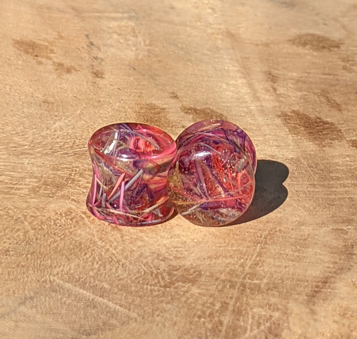 Pink and purple resin ear gauges on a wooden surface