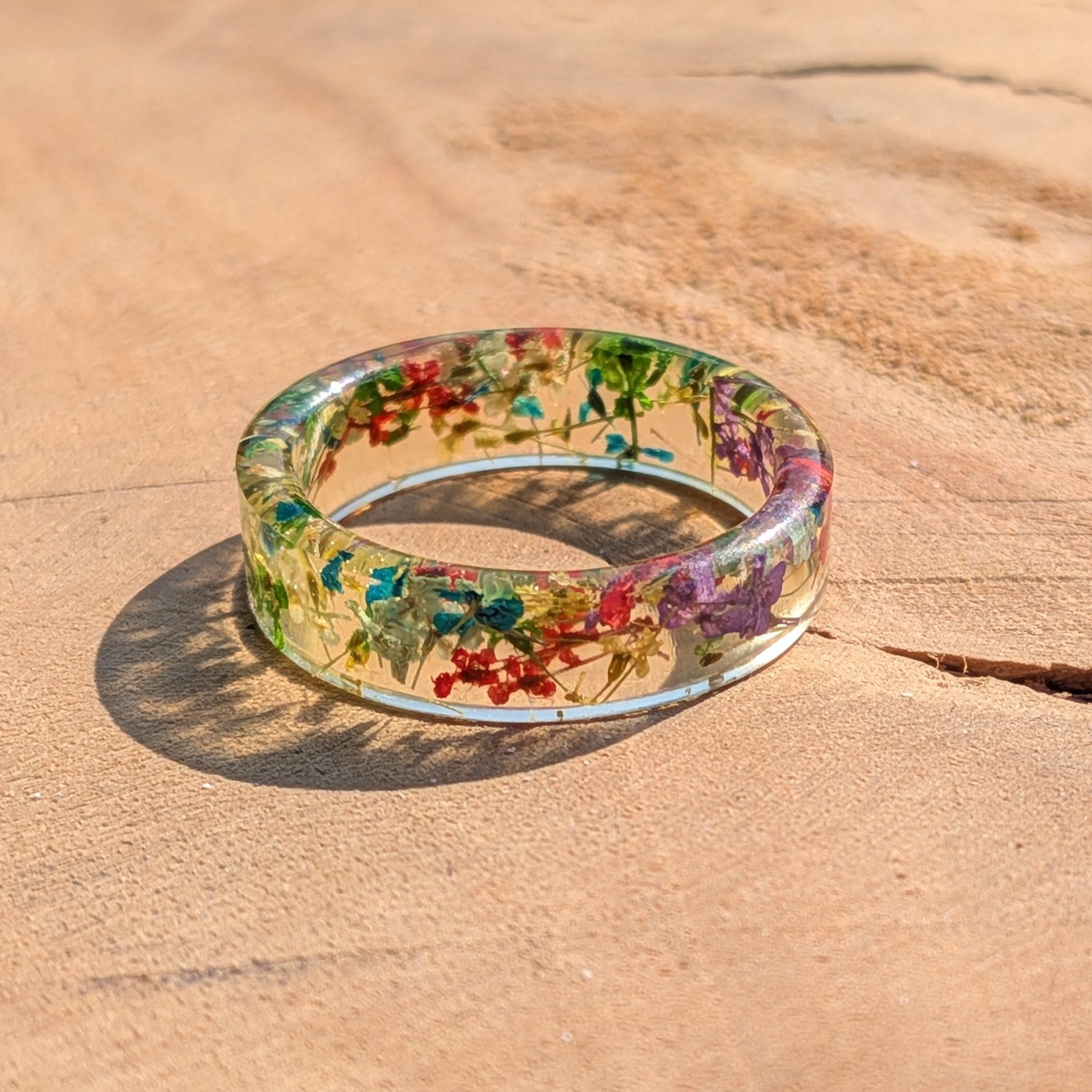 Clear resin ring with floral embedded stones on a sandy surface