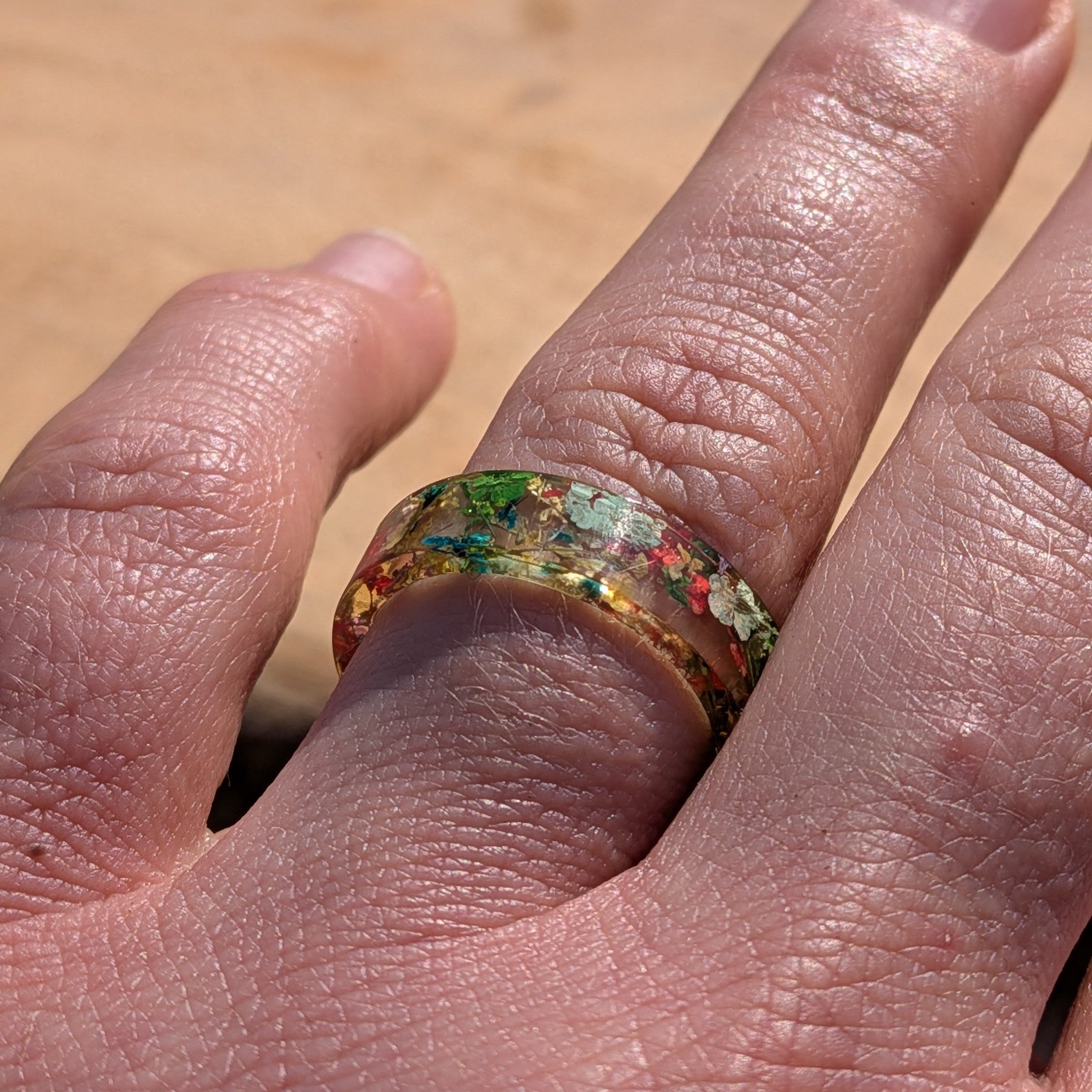 Close-up of a hand wearing a colorful ring with a wooden background