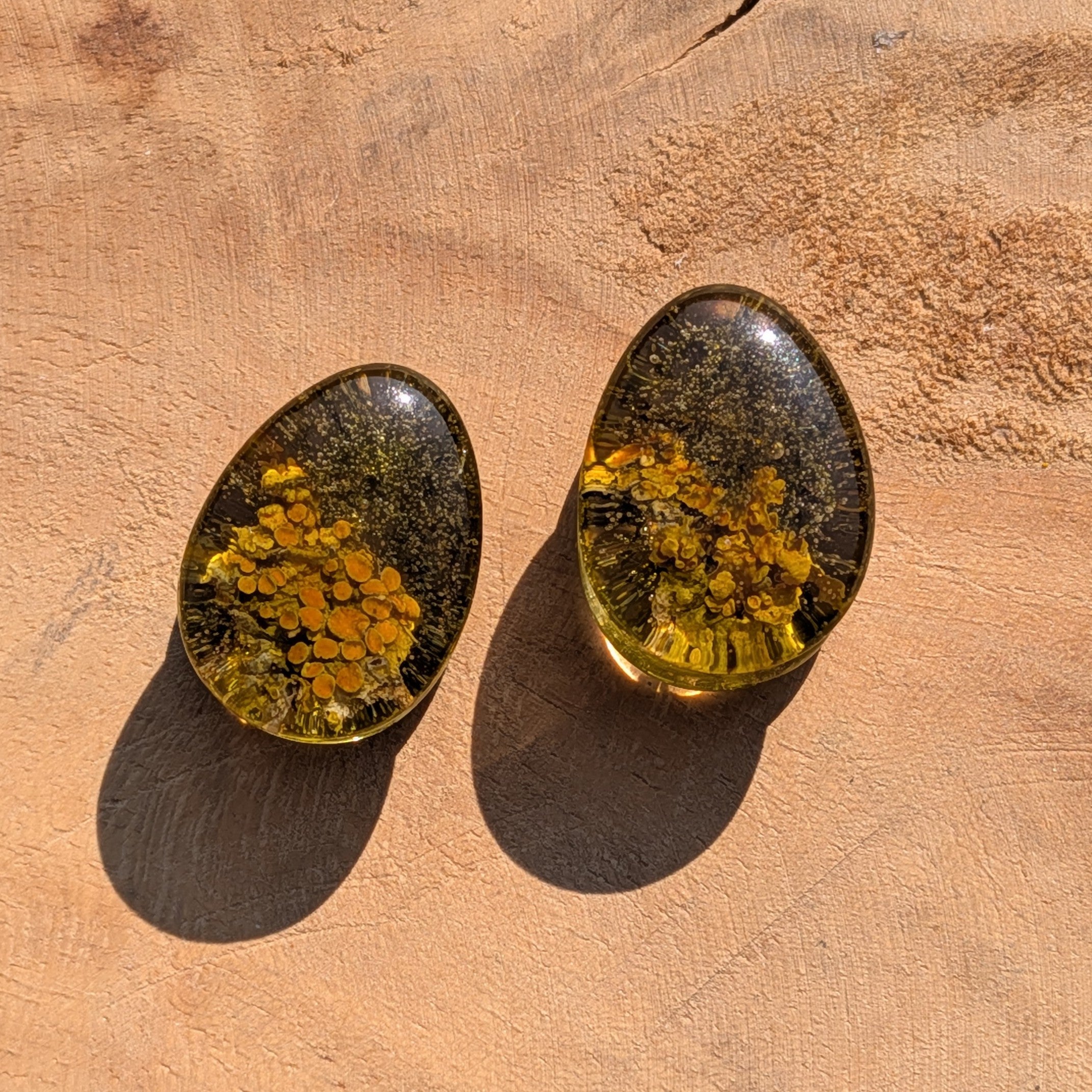 Two oval-shaped earrings with embedded yellow stones on a brown surface